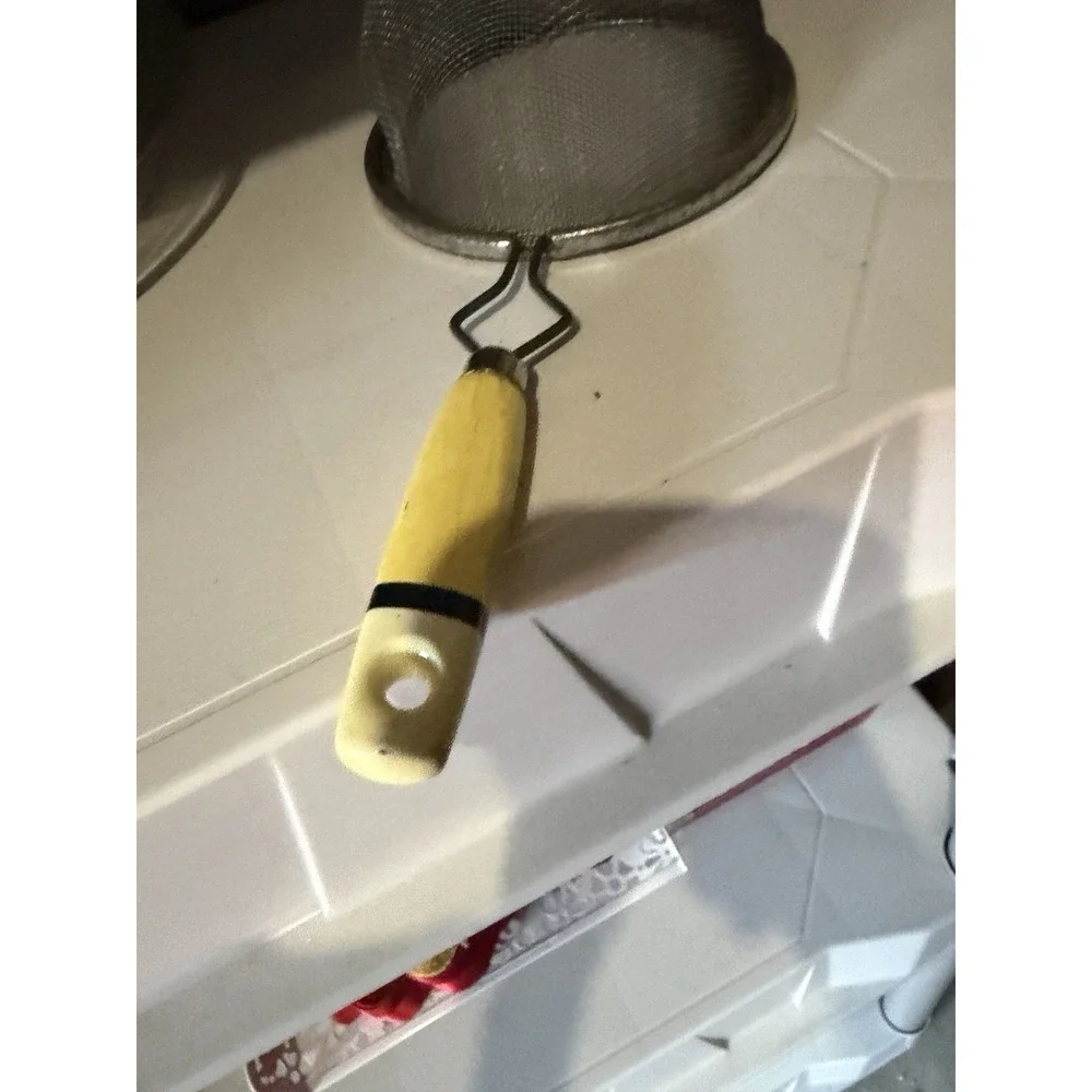The vintage Eckoline hand-held mesh strainer with a yellow and white plastic